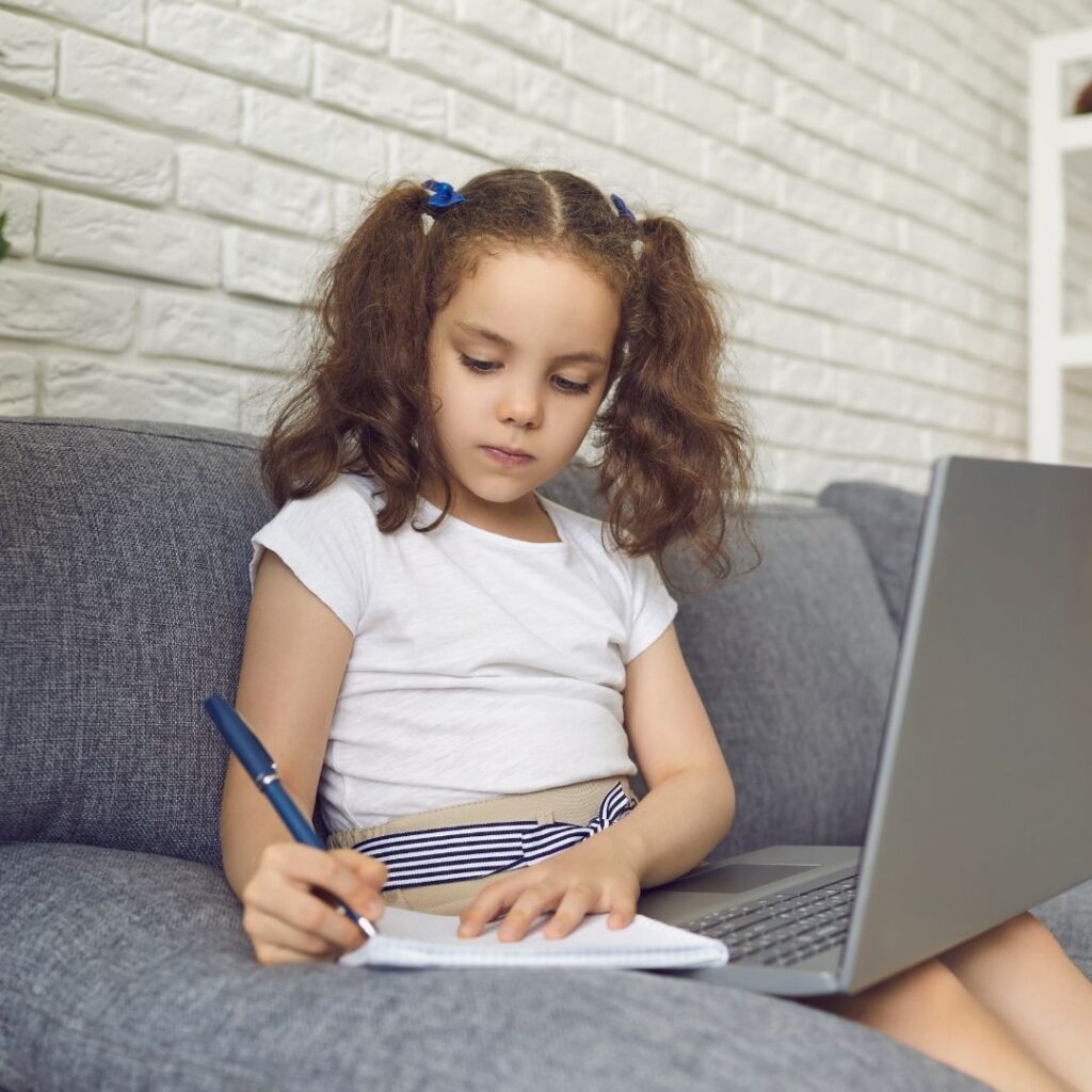 little girl writes and looks at computer 