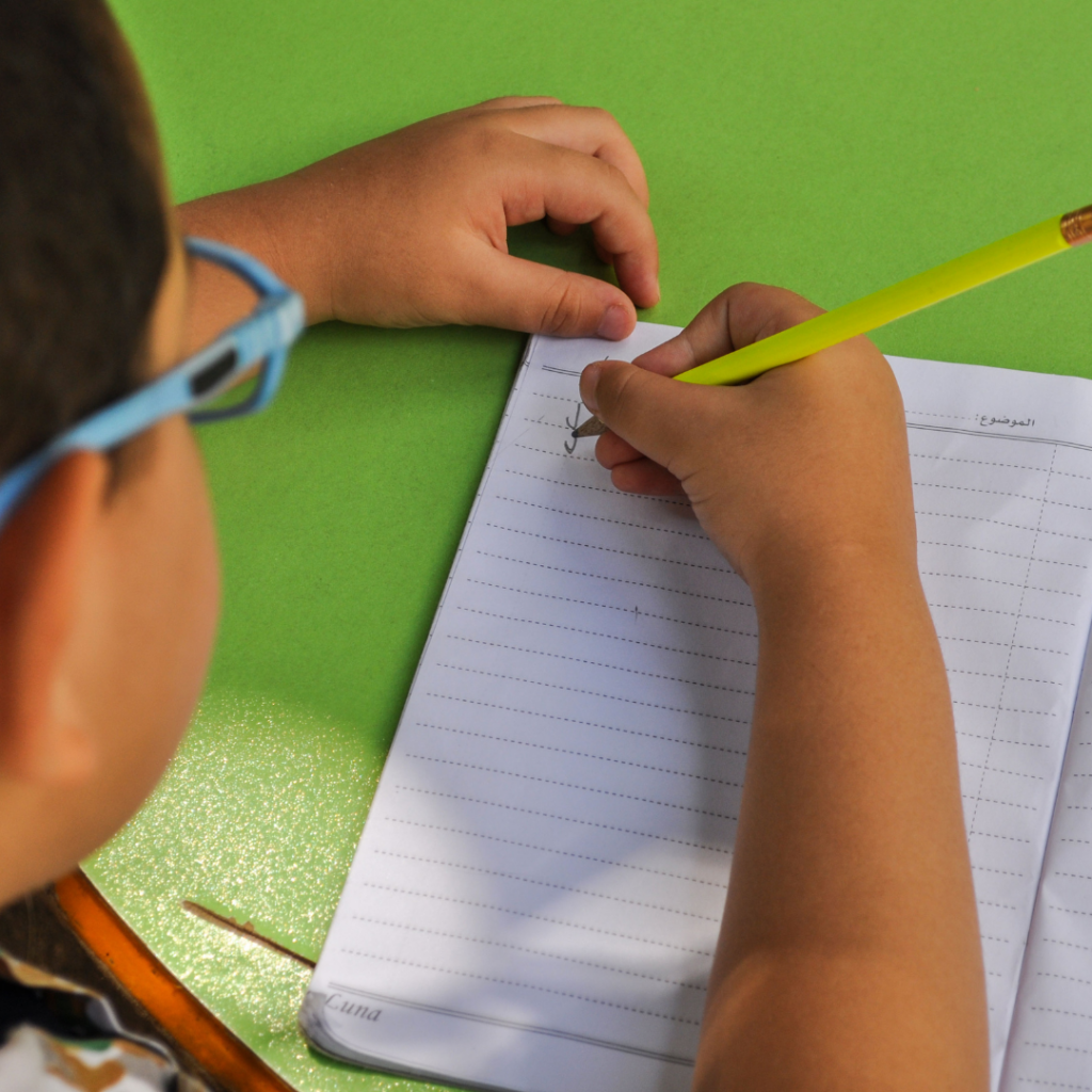 a kid with blue glasses writing with a yellow pencil